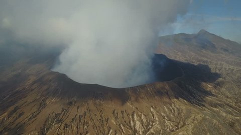 Flying towards the edge of the Mount Bromo volcano, billowing thick white grey smoke, rugged scenery Indonesia