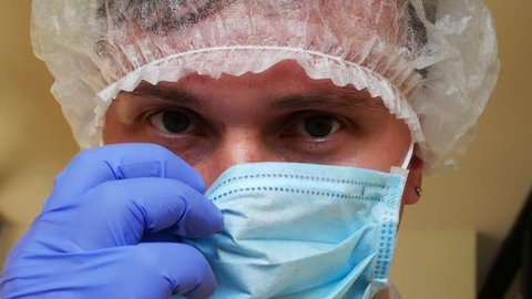 Laboratory Assistant in Medical Mask, Sterile Gloves and in Medical Dressing-gown in Laboratory on Smiles After Long Working Day Over Research Wuhan coronavirus 2019-nCoV or COVID-19