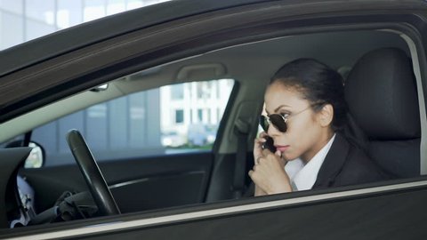 Lady in sunglasses, sitting in car and talking over cellphone, police agent