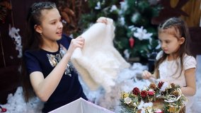 Two little girls at a Christmas tree prepare a gift for the grandmother. Granddaughters pack a white shawl as a present to their beloved grandmother in a gift box. - Powered by Shutterstock - Get 15% off with code: PIKWIZARD15