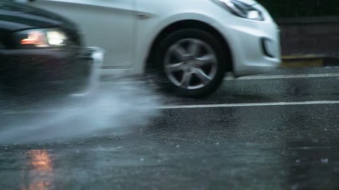 Rain in Rush Hour. The car moves past the camera and rides through the puddle. From under the wheel rises a beautiful stream of water. Filmed at a speed of 240fps