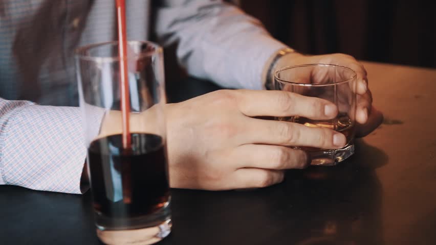 Hands of unrecognisable man in plaid shirt holding glass of whiskey upon table with cola at bar | Shutterstock HD Video #29445778