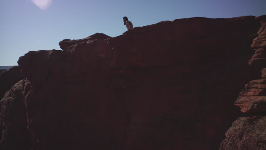 Young bearded hipster man runs and jumps off rock, Utah lake reservoir, mountains and sky, Summer 2017