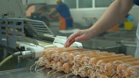 Food warehouse. Worker`s hands operates automated production line producing sausages. Sausage after going through production line is taken by worker and put on table. close up. Shot in 4k