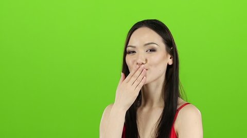 Girl in a red dress flirts, sends kisses and smiles. Green screen. Slow motion