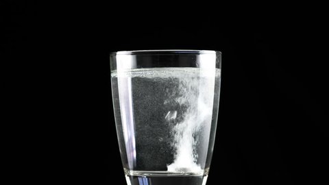 Effervescent antacid tablet in glass of water on black background with rotating
