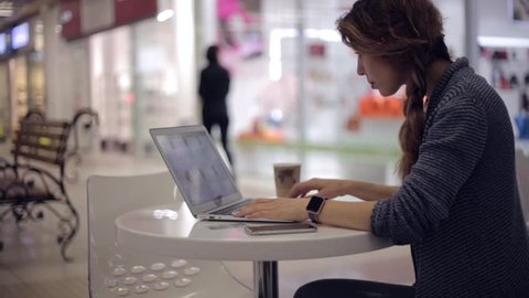 Attractive woman working laptop in a shopping center. A woman is looking in the online store for a new watch