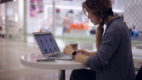 Young woman is looking in the online store for a new smart watch using a notebook