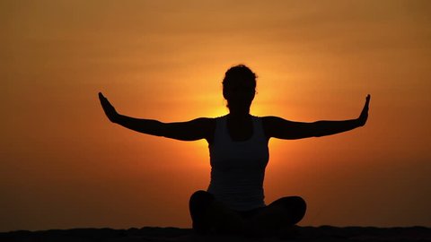 Healthy woman meditating in pose lotus over orange sun