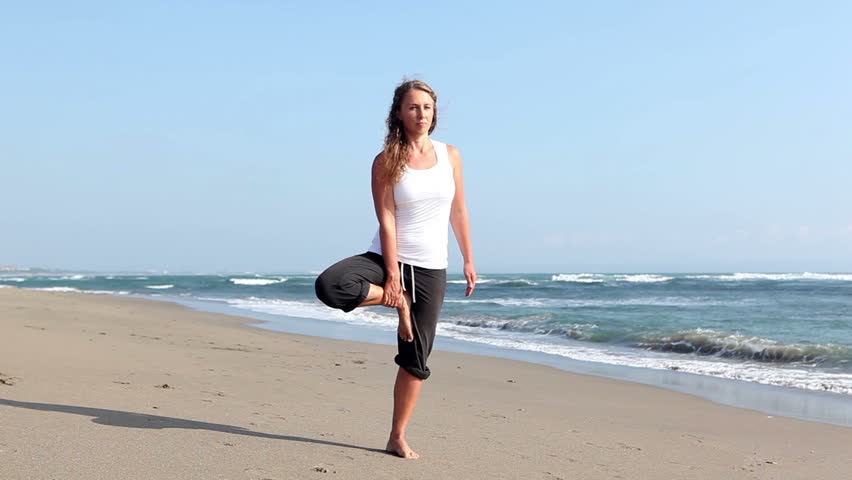 Peaceful young female practicing yoga on beach