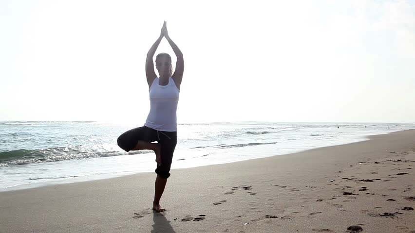 Peaceful young female practicing yoga on beach