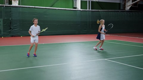 Two happy children serving and returning balls training skills on court with rackets. Pretty boy and girl playing sport game in recreation area. Future professional players having tennis lesson.