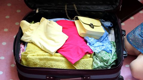 A happy young woman is going to rest on a trip and summer things and shoes are put together in a suitcase. The concept of travel.