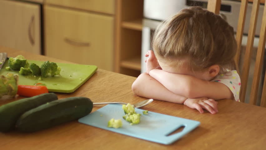 Portrait of a little girl in the kitchen. Mom gives the daughter a broccoli and a carrot. The girl pushes the vegetables away. Healthy food. Childish whims. Royalty-Free Stock Footage #29468866