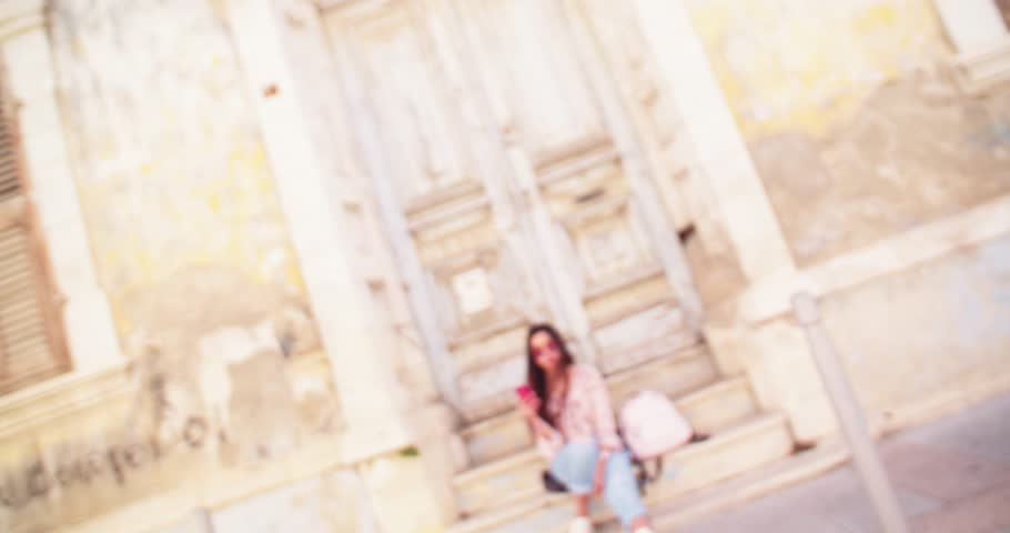 Hipster teenage tourist girl with mobile phone sitting on doorstepss in European antique city