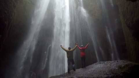 Young happy couple standing under beautiful waterfall Gljufrabui in Iceland and raises hands, feeling freedom and joy 库存视频
