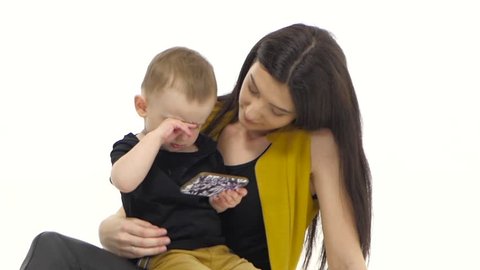 Woman is sitting on the floor with her baby, she is stroking his hair. White background. Slow motion