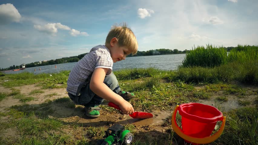 Cute caucasian child, baby kid boy plays with toys on the sunny river bank. Recreation and entertainment. Happy positive childhood memories. Growth and development of the kid