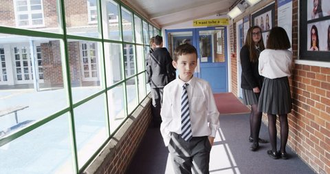 4K Little boy isolated & outcast at school walking through hallway with other kids staring