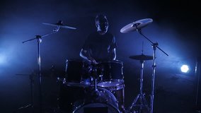 The drummer plays the drum set on the stage. Shot in a slow motion. Music video punk, heavy metal or rock group.