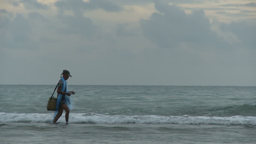 A fisherman tends to his net as he walks from left to right the stops to face