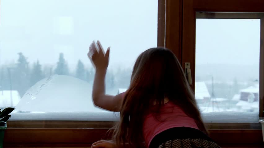 Girl winter draws a finger on the glass window at home.