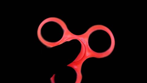Pinwheel spinner fidget red color in the hands is spinning on a black background. Toy anti-stress relaxation. Soothing and distracting object for  tranquility.
