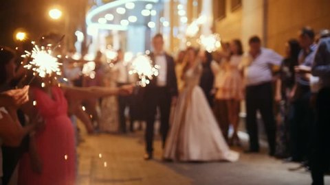 Wedding fireworks - sparkler in hands on a wedding - bride, groom and guests holding lights in, de-focused and slow-motion