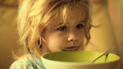 Breakfast child eats. Healthy diet for toddler. Cute boy with beautiful hair at home at table with spoon porridge or rice. Child eating oatmeal with milk. Concept healthy breakfast for children
