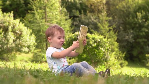 Young Baby Boy Using Smartphone Tablet Outside At Park.