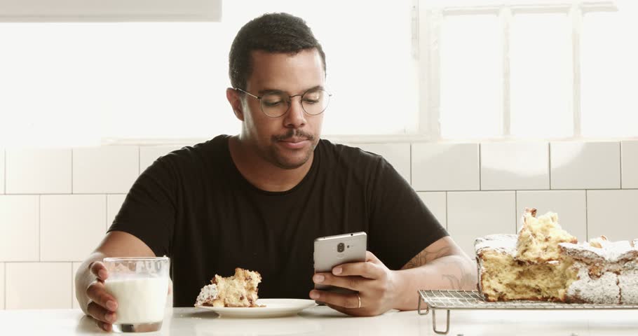 mixed race black man has a breakfast with milk and cake and talking by phone in a sunny loft space