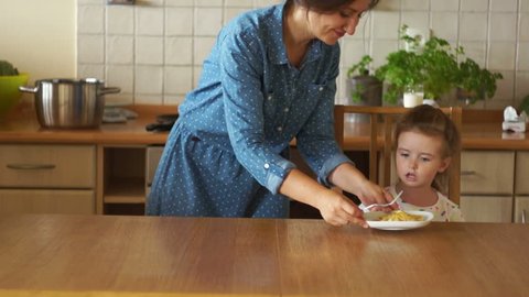 Mother and daughter having healthy breakfast in kitchen. The girl is not hungry. She refuses to eat, pushes the plate aside. Poor appetite.