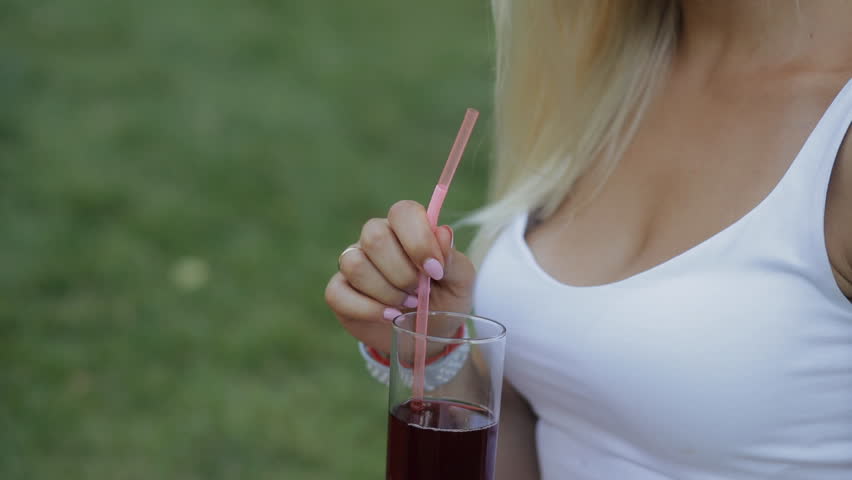 Healthy lifestyle food. Young woman drinking fresh garnet juice sitting outdoors at meadow in slow motion