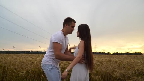 A guy with a girl in his arms is spinning in a wheat field at sunset.