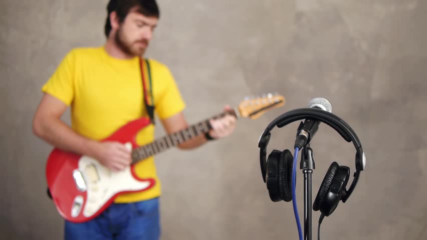Musician playing song on guitar with headphones and microphone in front