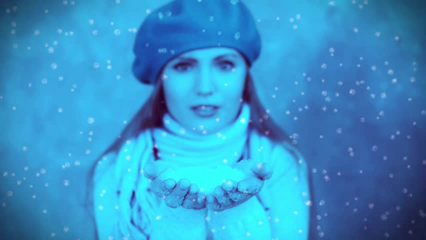 Beautiful woman in scarf blowing snow during snowfall