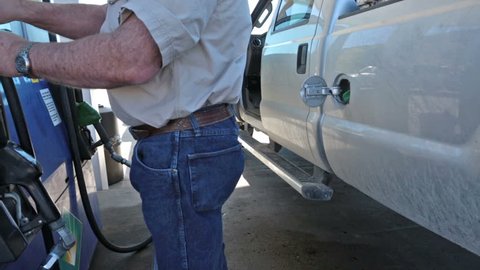Man filling gas into pickup truck. Person at station re fuel for a road trip. Expensive cost of living caused by environmental regulations. Need for USA to become energy independent.