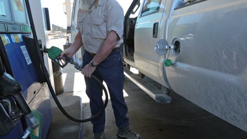 Man filling pickup truck with gas. Person at station re fuel for a road trip. Expensive cost of living caused by environmental regulations. Need for USA to become energy independent.