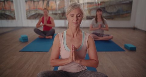 Beautiful retired woman relaxing during meditation exercise at a yoga class in a fitness studio