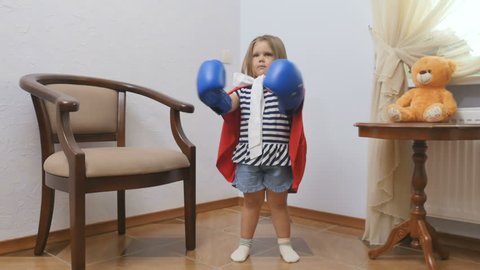 Cute little girl in boxers gloves and in red cloak show her power as superhero