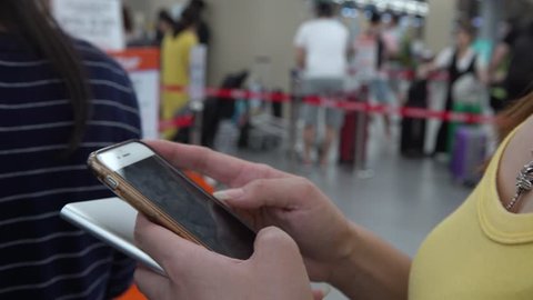 4K Asian tourist woman checks phone as waits for Check-In Counters at International Airport. People using smartphone do quick text messaging with friends social network on travel vacation holidays-Dan