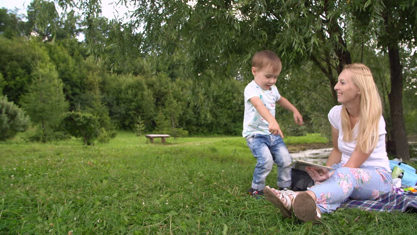 Young mother and little son spending day in the park. Woman and child using tablet computer.