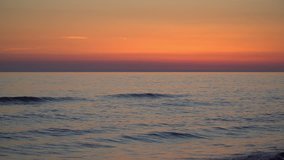 Romantic motion background video of calm sea at sunset, deep orange and purple colored sky