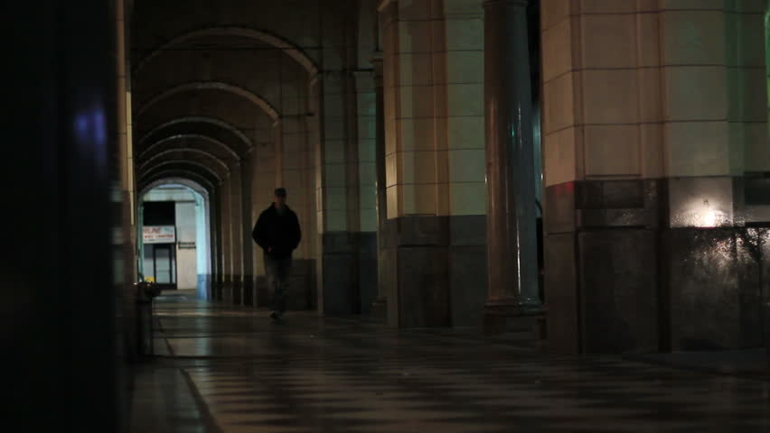 A man walks down a dark arched pathway at night alone