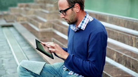 Portrait of young man with tablet computer sitting on the stairs, outdoors
