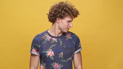 Young crazy guy with curly hair shaking head and screaming while standing isolated over yellow background