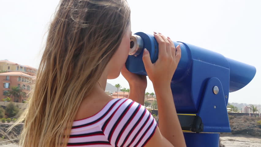 Tenerife. Spain. Beautiful blond girl on vacation observes Costa Adeje, Las Americas through a telescope on the viewpoint.
