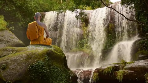 Buddhist monk in meditation at water fall on the mountain.