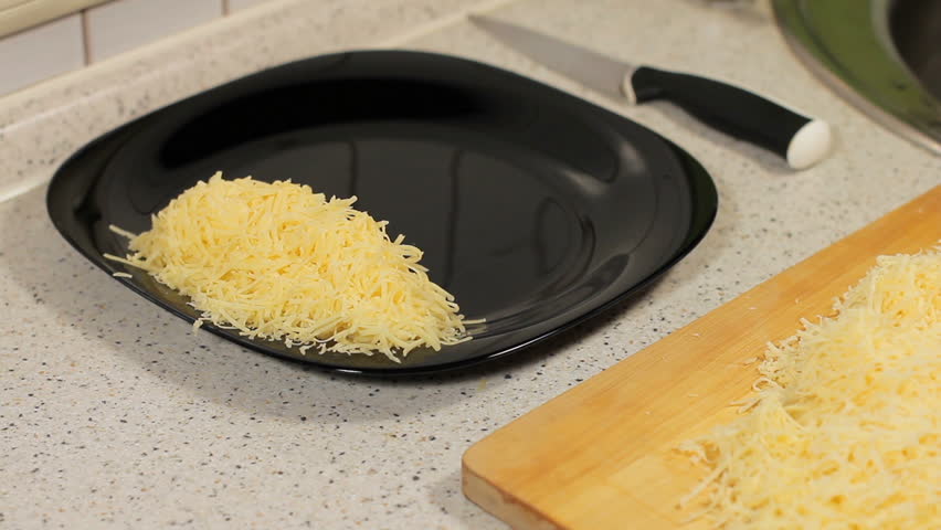 female hand shifts are fresh grated cheese in a plate. Woman grating cheese. preparation of pizza