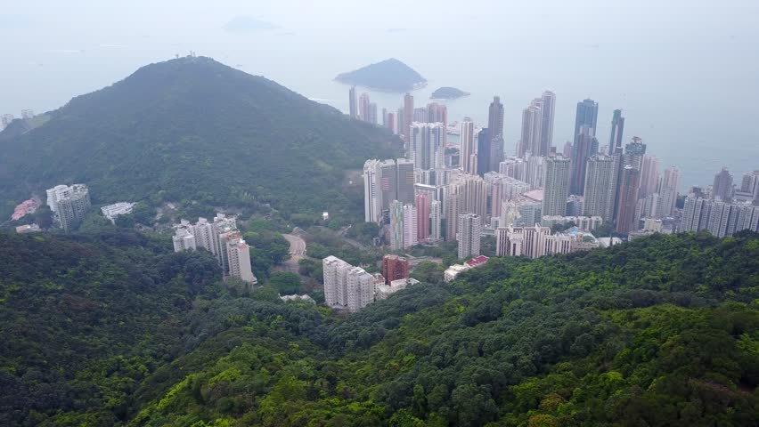 Green mountainous landscape and urban Kennedy Town at north west side of Hong Kong Island, aerial shot in foggy day. Forested slopes and gaps, Mount Davis peak seen ahead. Dense build city area